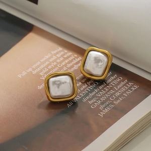 Macro shot of gold square frame faux pearl earrings placed on a fashion magazine