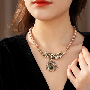 Detail of vintage rose gold pearl necklace with crystal leaf pendant and green gemstone
