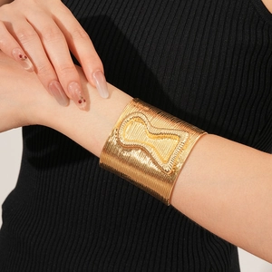 Detail of gold wide open cuff bracelet with vertical linear texture and hourglass motif