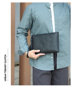 Close-up of black woven leather clutch bag with wrist strap in urban outdoor setting