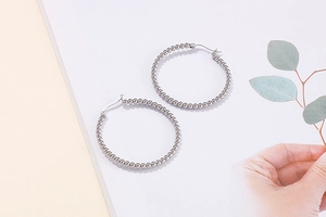 Detailed view of silver stainless steel beaded hoop earrings on a minimalist background