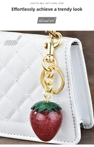 Detail of red glitter strawberry keychain charm on a white quilted luxury handbag