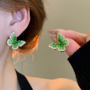 Detail of 18k gold butterfly stud earrings with green stones and sparkling crystals