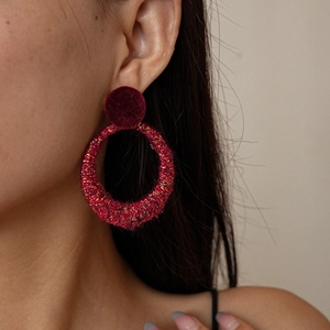 Close-up of burgundy fuzzy knit round drop earrings worn by a model in soft lighting