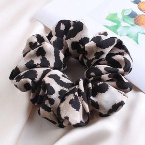 Close-up of a soft leopard print fabric scrunchie on a glossy satin background detail