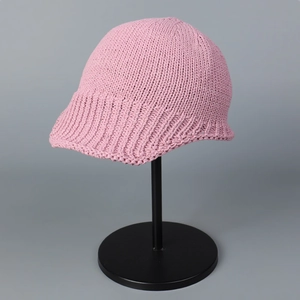 Detail of pink knitted pilot hat with thick yarn texture on black metal display stand