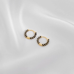 Detail of gold hoop earrings with black enamel spiral texture on white silk background