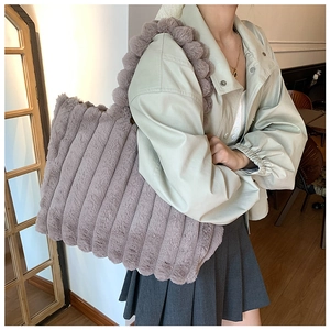 Detail of grey-purple plush tote bag with striped texture and decorative pom-pom on strap