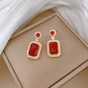 Detailed macro view of ruby-red rectangular earrings on a luxury champagne silk background