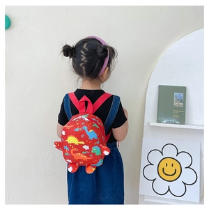 Detail view of children's red backpack with cartoon dinosaur print on a toddler's back
