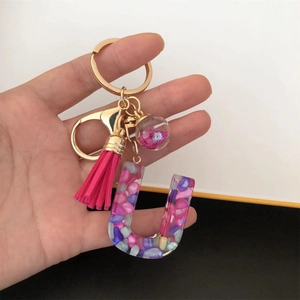 Detail of resin letter U keychain with colorful stones, pink tassel and glitter ball