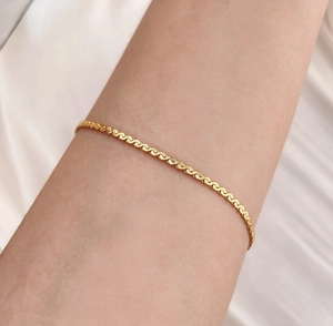 Dettaglio del bracciale a catena serpente dorata al polso su morbida seta bianca