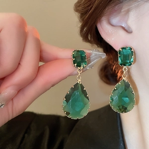Detailed view of emerald green teardrop earrings with gold textured borders on a model