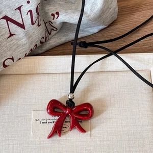 Gros plan du pendentif nœud rouge poli sur cordon noir sur une surface texturée
