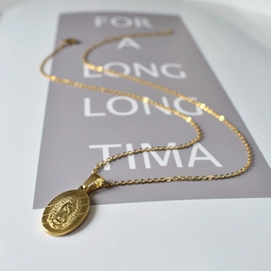 Détail d'un collier doré avec pendentif ovale Vierge Marie posé sur une carte minimaliste