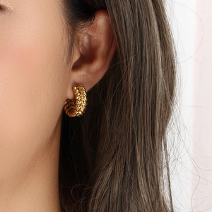 Detail shot of a model wearing gold plated C-shaped earrings with wheat pattern texture