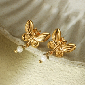 Detailed close-up of golden butterfly earrings featuring elegant round pearl pendants