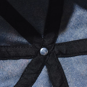 Close-up of denim baseball cap interior featuring black cross-taped seams and metal rivet