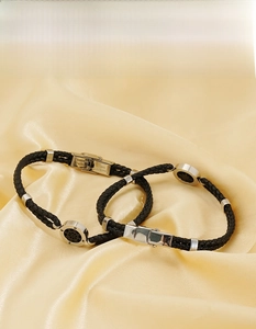 Macro detail of black braided leather bracelet featuring a silver compass charm and clasp