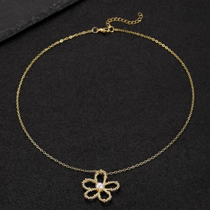 Detail of gold flower necklace featuring a central pearl on a black textured background
