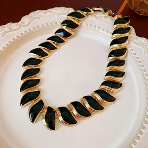 Détail de collier vintage doré et émaillé noir posé sur une assiette en céramique