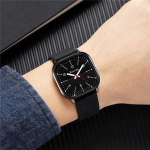 Close-up of square black watch dial with silver markers on a leather strap and denim