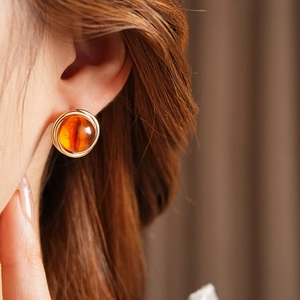 Close-up of golden round stud earring with amber resin stone on model's ear