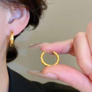 Macro detail of gold-plated hoop earrings with textured finish and secure clasp