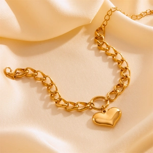 Golden chunky curb chain bracelet with polished heart pendant on champagne silk background