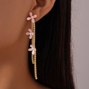 Macro detail of long gold tassel earrings with pink resin flowers and zircon crystals