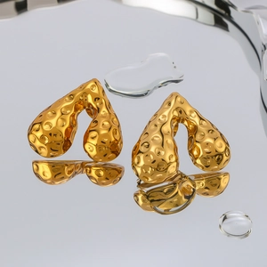 Hammered heart-shaped 18K gold plated stainless steel earrings on reflective surface