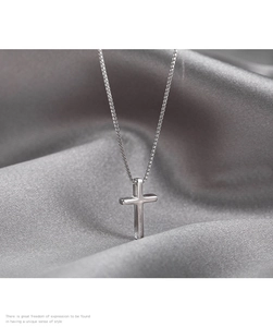 Macro detail of silver cross pendant with box chain on elegant grey satin background