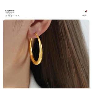 Close-up of chunky gold-plated hoop earrings with a high-polished mirror finish on a model