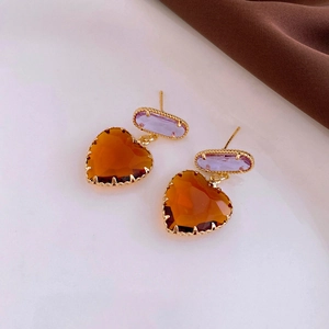 Detail view of heart-shaped amber crystal earrings with purple oval gems on silk