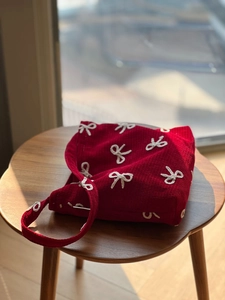 Close-up of red corduroy shoulder bag with white bow embroidery on a wooden stool