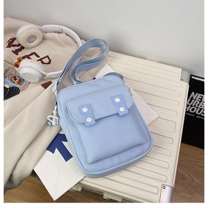 Detail of light blue canvas crossbody bag with white buttons on a cream suitcase