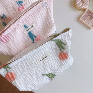 Détail de la broderie tulipe sur des trousses de maquillage en tissu texturé avec zip
