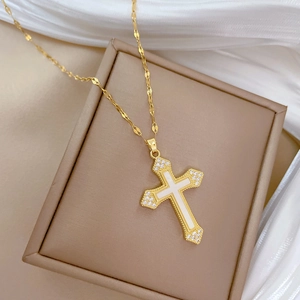 Detail of gold titanium cross pendant with shell inlay and diamonds on beige jewelry box