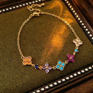 Detail of gold-plated clover bracelet with colorful zircon stones on green padding
