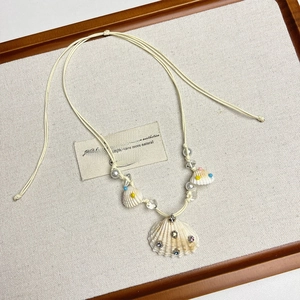 Detail of bohemian woven beige cord necklace with natural shell and faux pearl charms