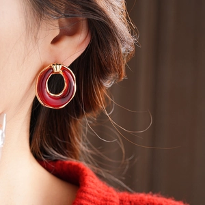 Close-up of model wearing gold hollow resin hoop earrings with deep red finish