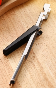 Close-up of a stainless steel bottle opener tool on a rustic wooden cutting board