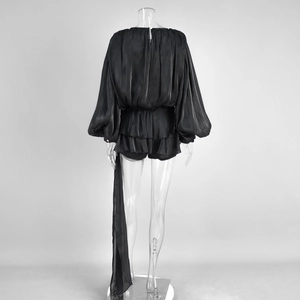 Detail view of the layered ruffle hem and flowing sash on the back of a black satin romper
