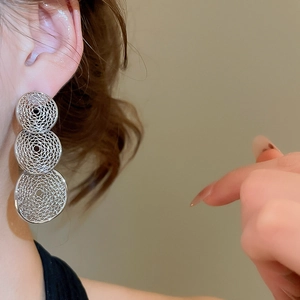 Detail of silver layered hollow geometric earrings on model showing textured wire design
