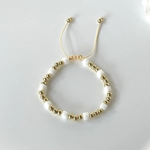 Adjustable beaded bracelet with gold round beads and white square crystals on a cream cord