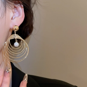 Detail of layered gold hoop earrings with white pearl pendant worn by a model