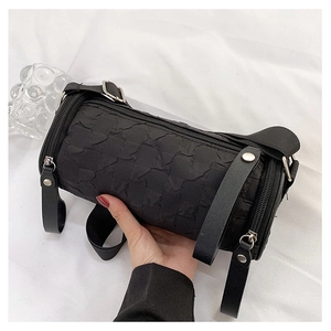 Detail showing the textured bubble fabric and metal zipper of the black cylinder bag