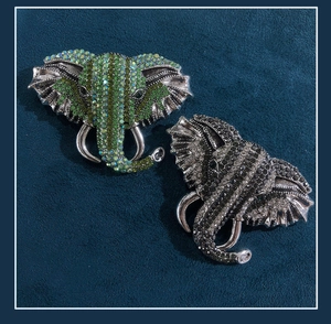 Detailed view of two elephant brooches with green and black rhinestones on blue velvet
