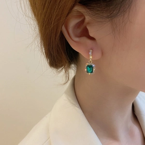 Close-up of elegant gold stud earring with emerald green gem and pavé diamond halo