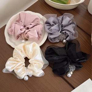 Detailed view of layered satin and organza scrunchies with pearls on a wooden desk